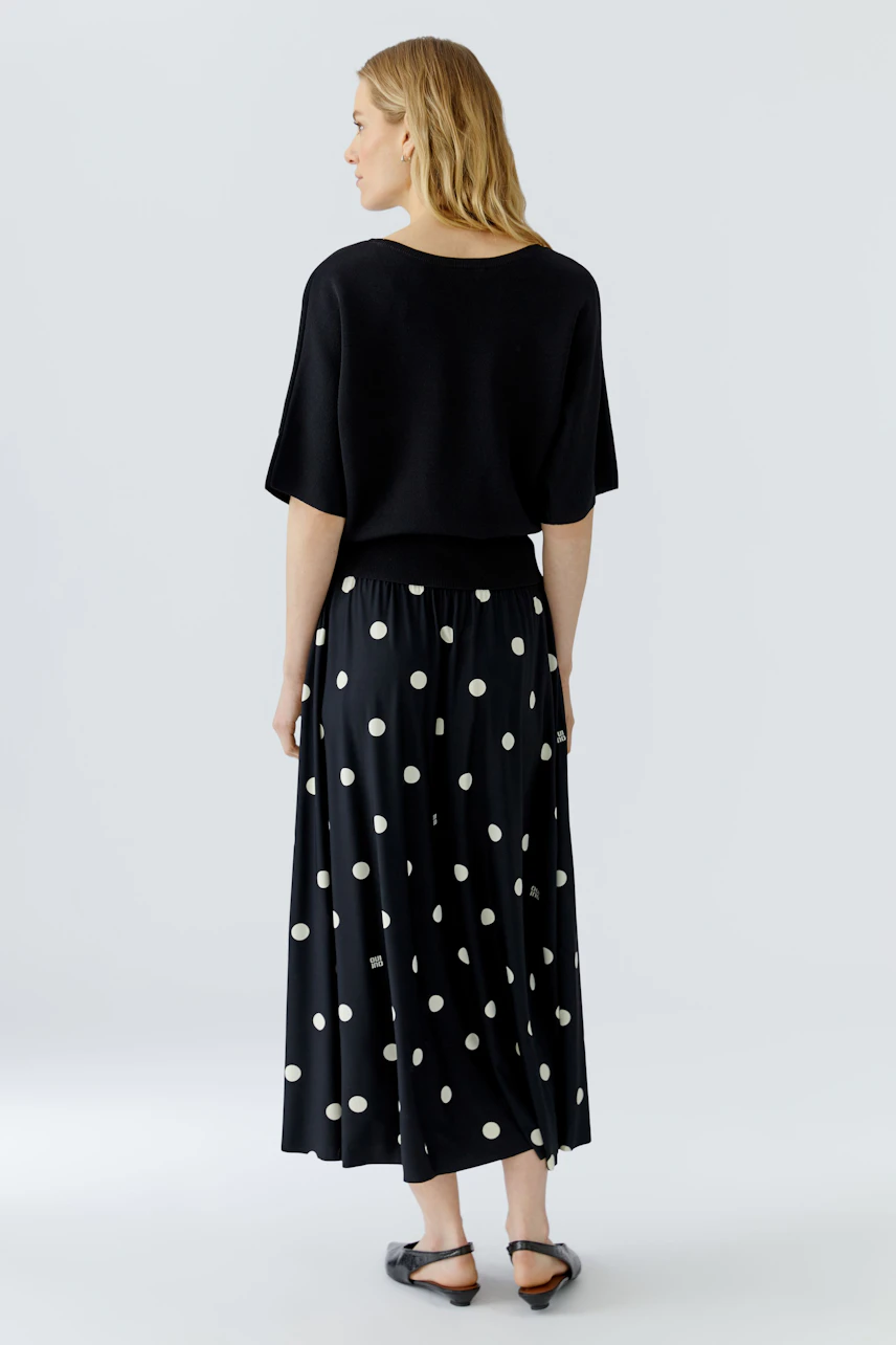 Casual pullover: Woman in a black pullover with short sleeves, paired with a polka dot skirt, seen from behind.