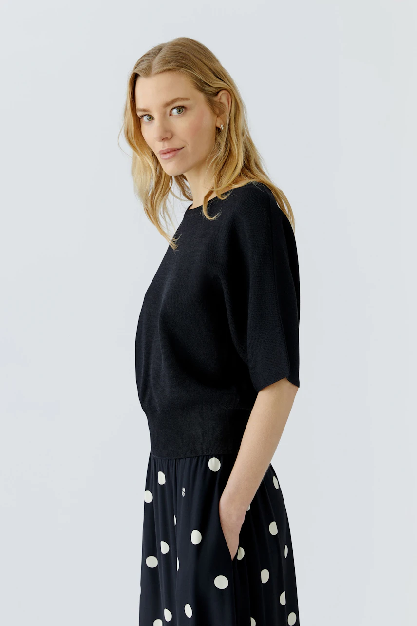 Casual women's pullover: Woman in a black pullover paired with a polka dot skirt, looking relaxed.