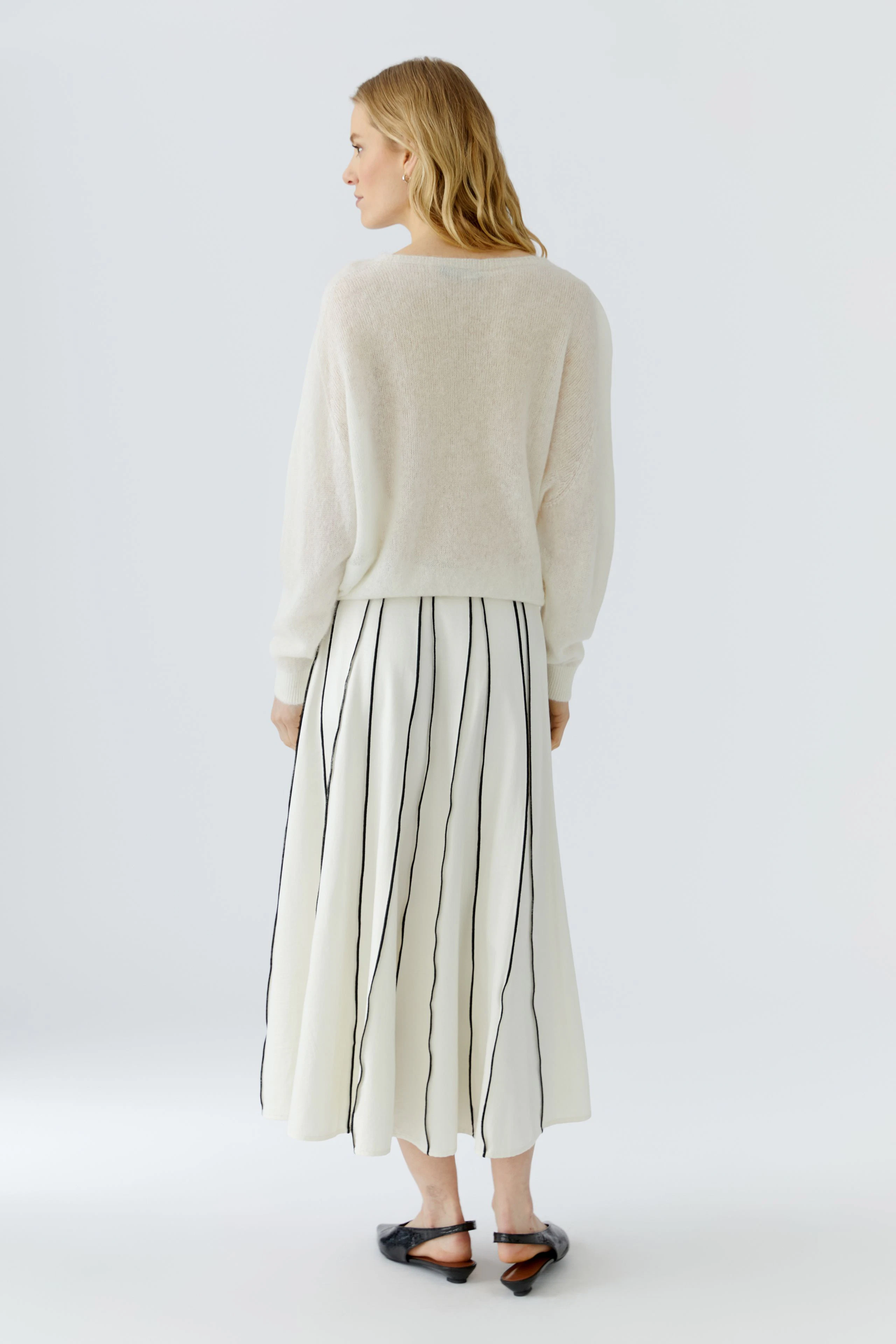 Frau im weißen Pullover und gestreiftem Rock, Rückenansicht. Schlichtes Design für lässigen Look.