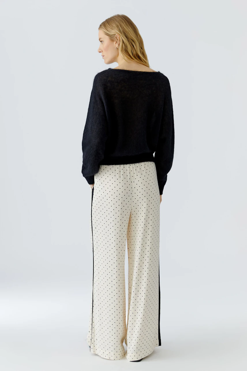 Frau im schwarzen Pullover, kombiniert mit weißer Hose. Lässiger Look, ideal für den Alltag.