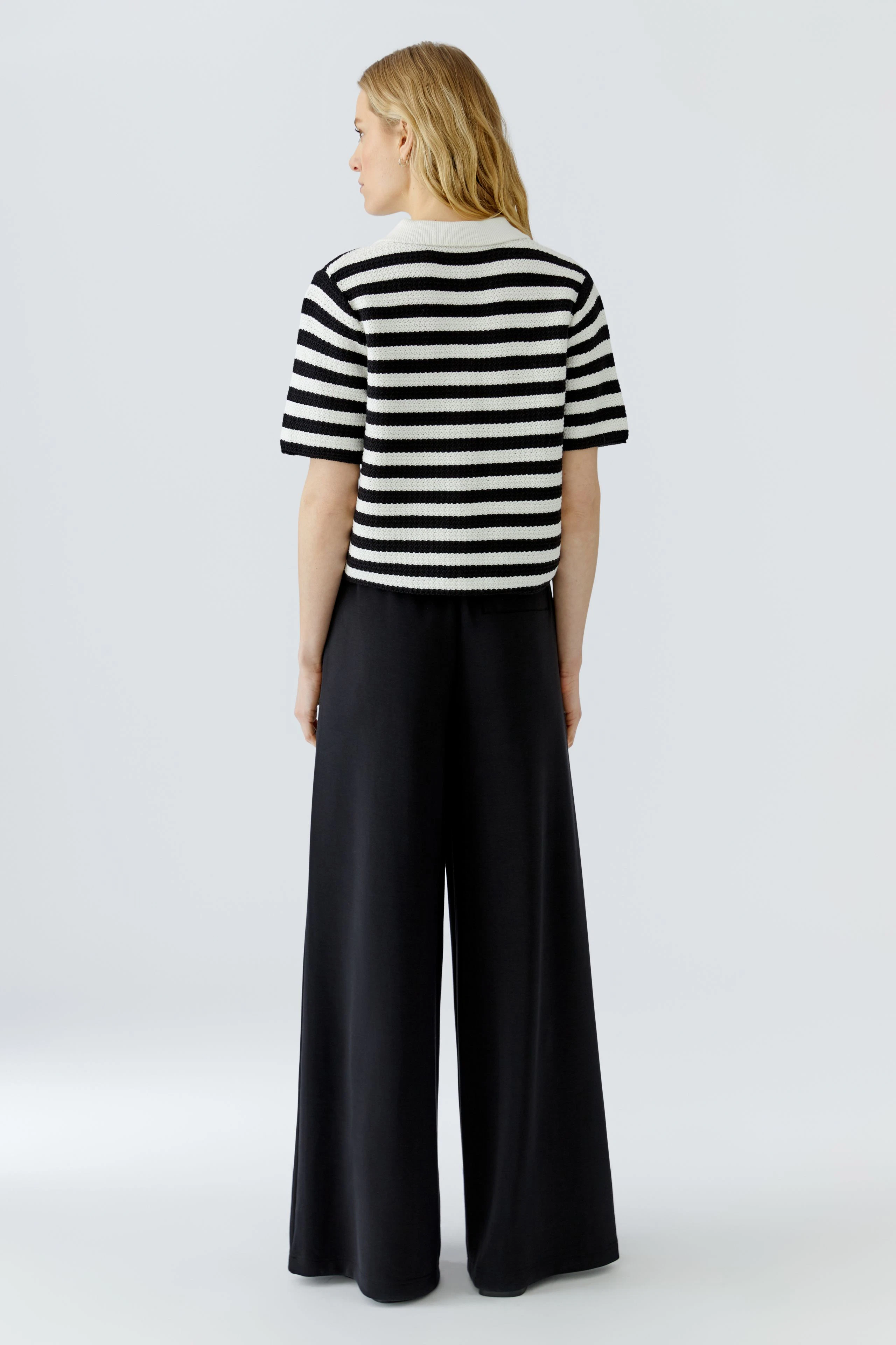 Striped cardigan: Woman in black and white striped cardigan with wide black pants, viewed from the back.