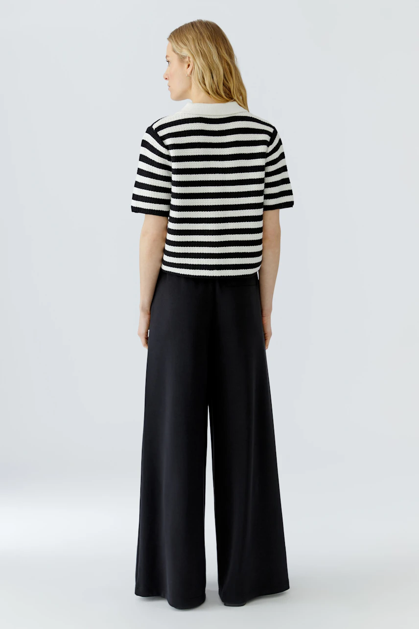 Striped cardigan: Woman in black and white striped cardigan with wide black pants, viewed from the back.