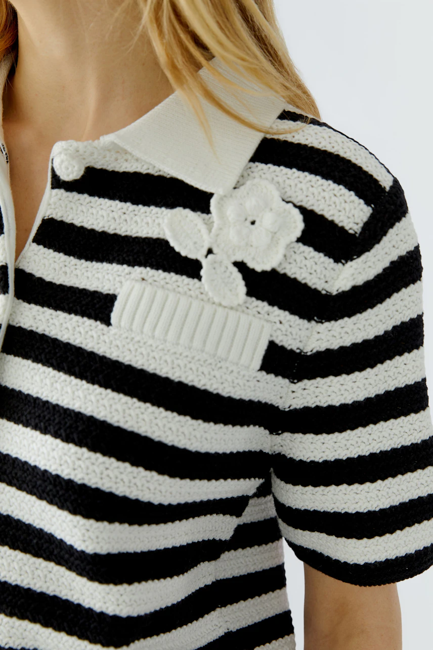 Striped cardigan: Woman in black and white striped cardigan with floral detail, casual and stylish.