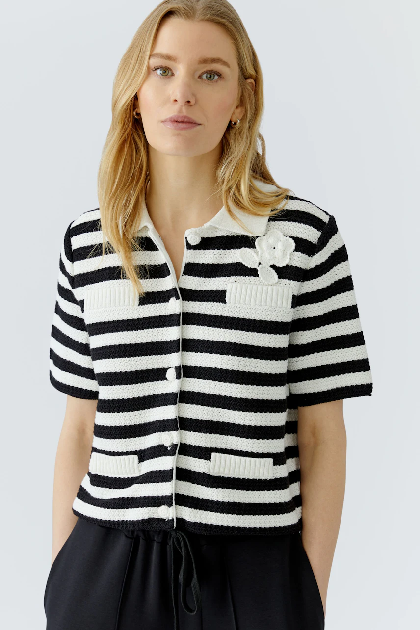Striped cardigan: Woman in black and white striped cardigan with floral detail, standing confidently.