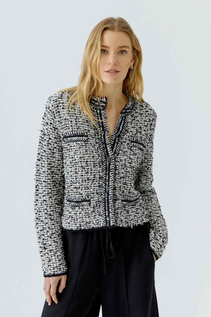 Casual knit cardigan: Woman in a textured black and white cardigan with relaxed black pants, looking confident.