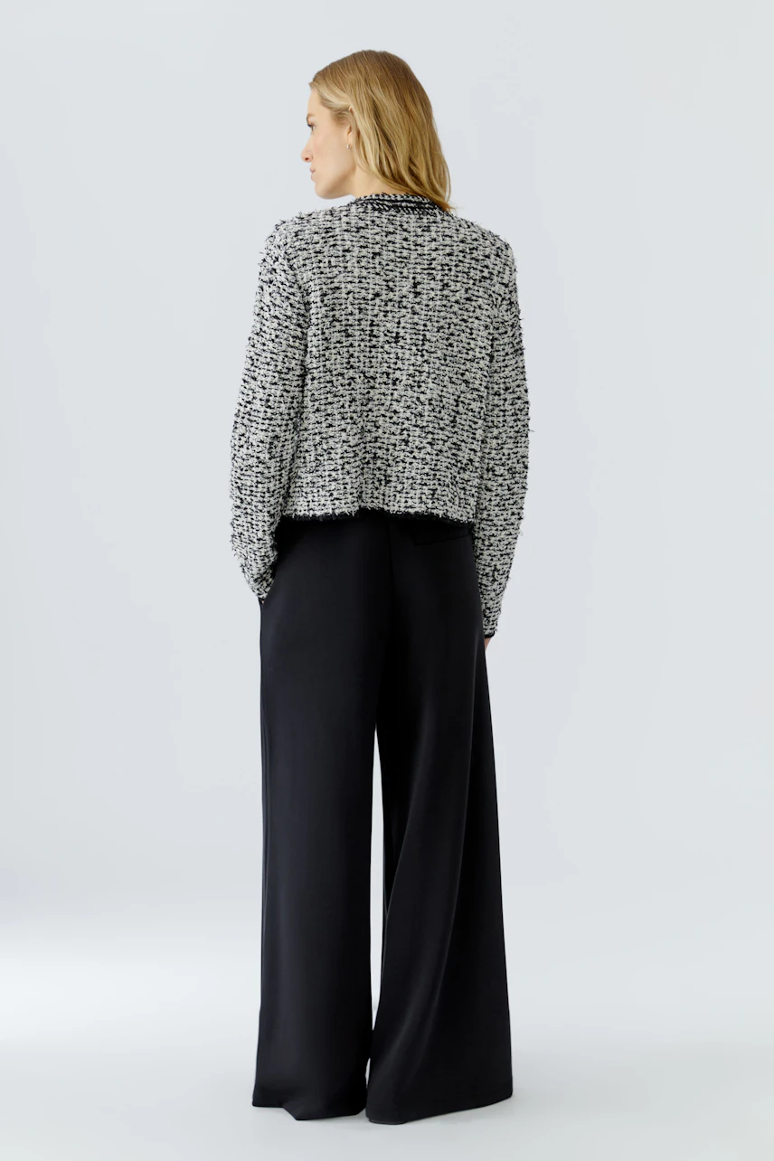 Woman in a textured knit cardigan, paired with wide-leg black pants, looking to the side.
