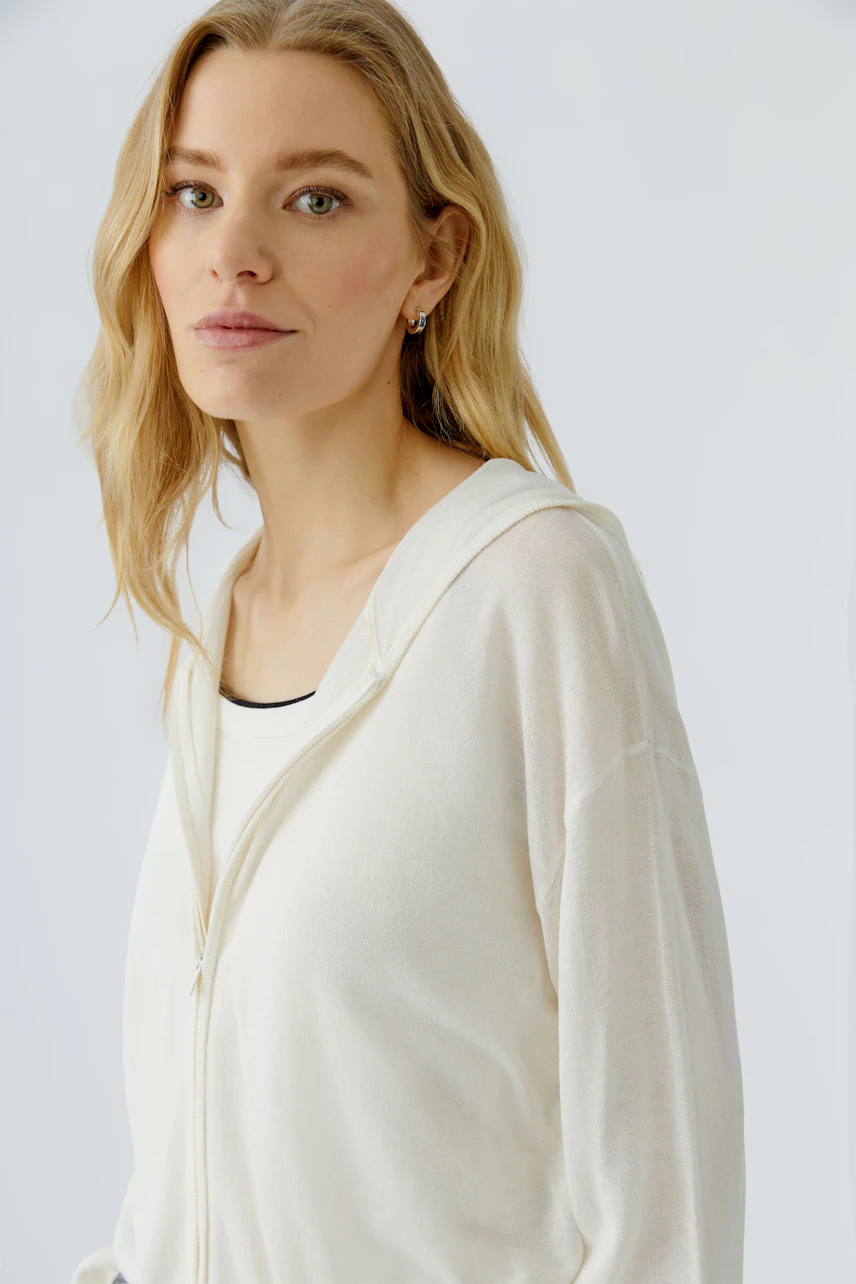 Frau in weißer Strickjacke: Lässiger Look mit Kapuze und Reißverschluss, ideal für den Alltag.