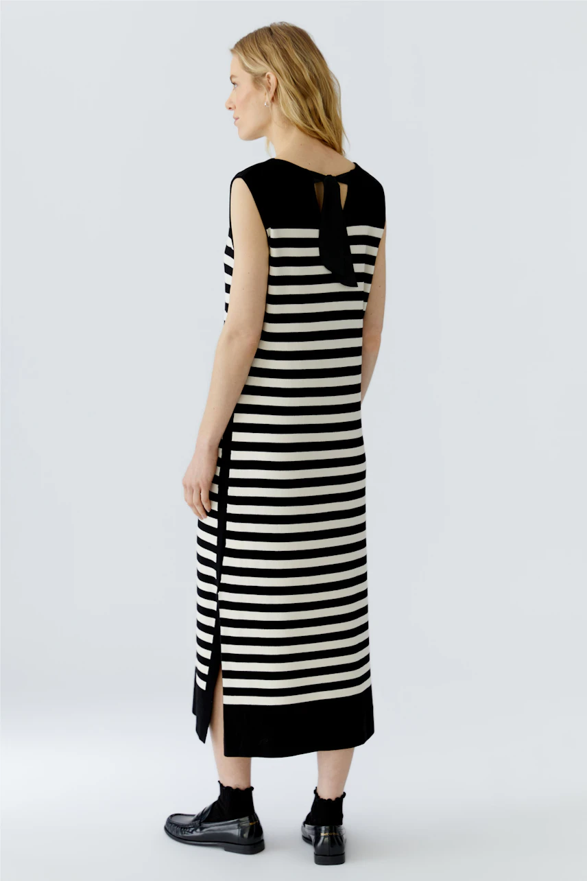 Striped dress: Woman in a sleeveless black and white striped dress with side slits, standing sideways.