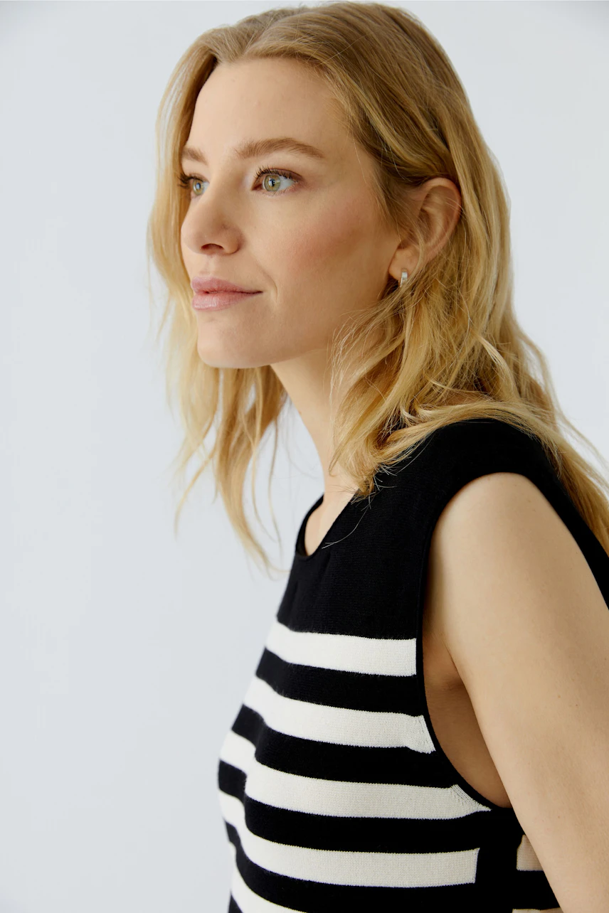 Casual dress: Woman in a sleeveless black and white striped dress, looking confidently to the side.