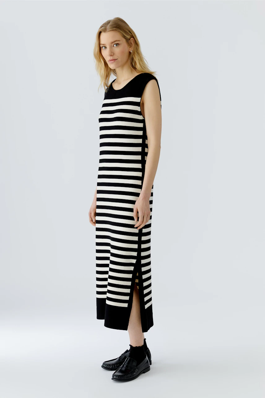 Striped dress: Woman in sleeveless black and white striped dress with side slits and black shoes.