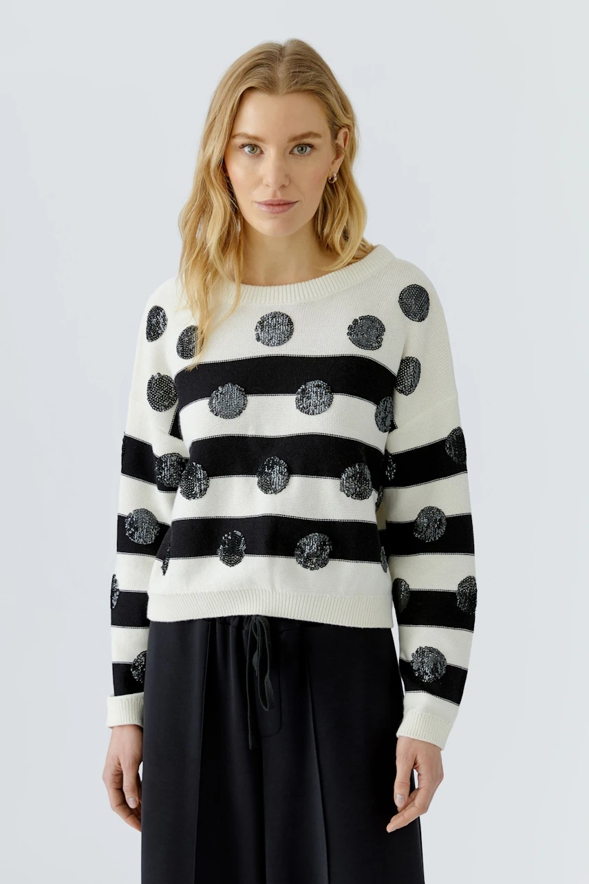 Casual women's pullover: Woman in a black and white striped pullover with polka dots, standing confidently.