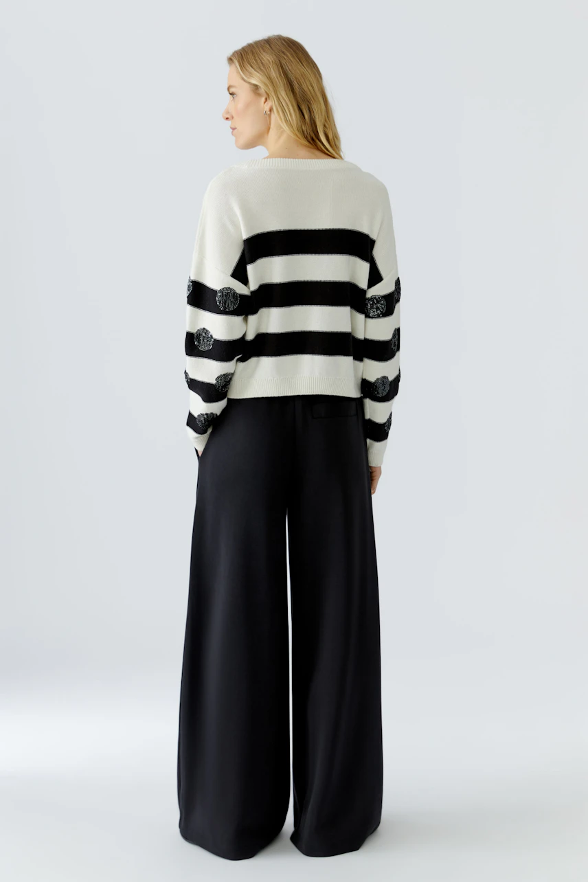 Casual women's pullover: Woman in a striped pullover with floral details, paired with wide-leg black pants.