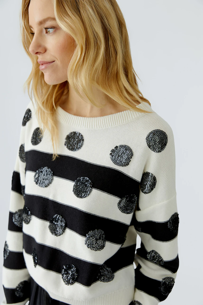 Casual women's pullover: Woman in a striped pullover with sequin dots, looking to the side.