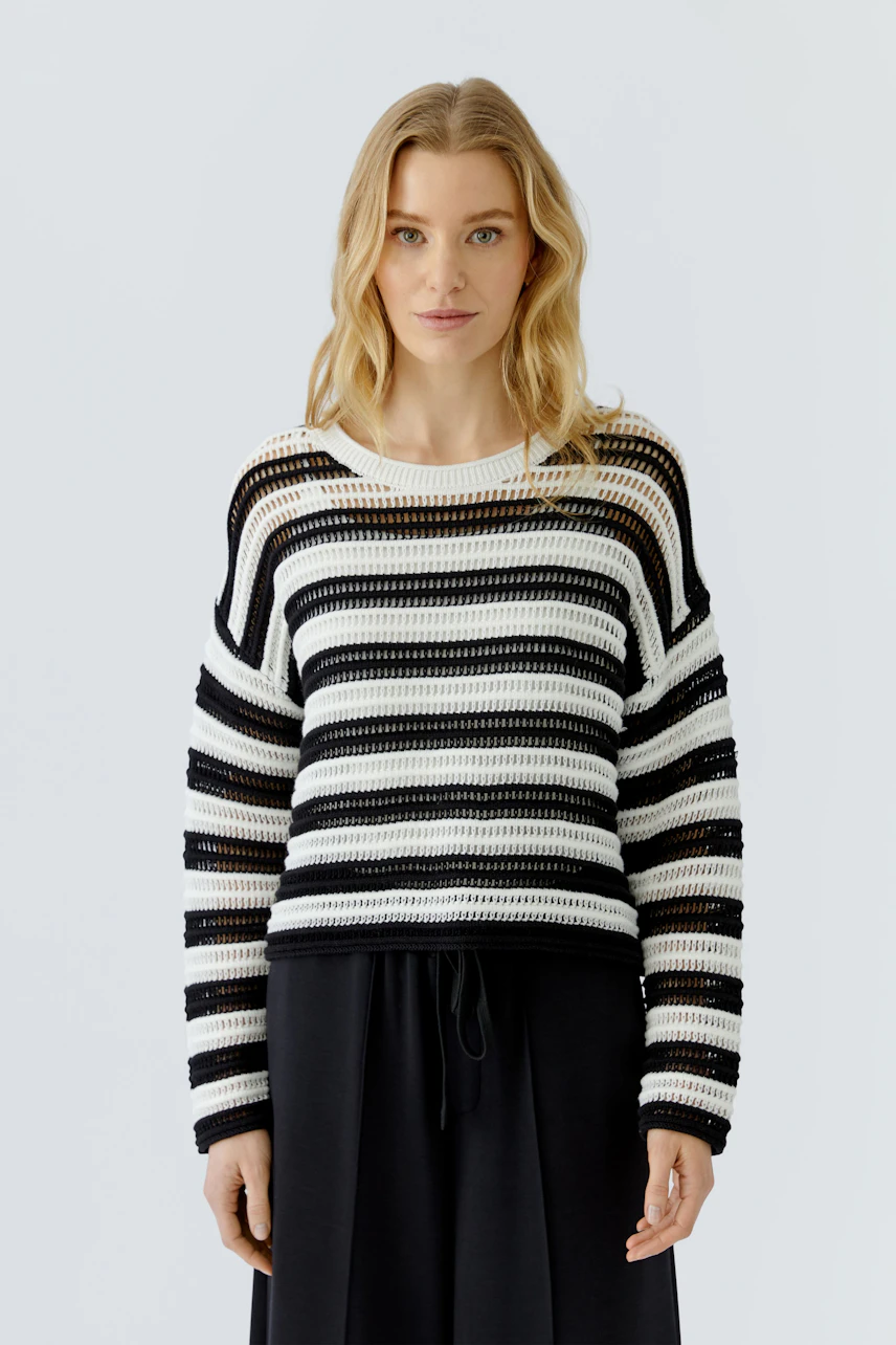 Casual women's pullover: Woman in a striped knit pullover with black and white pattern, standing confidently.