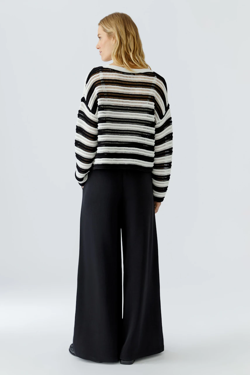 Casual women's pullover: Woman in a striped knit pullover with wide black pants, viewed from the back.