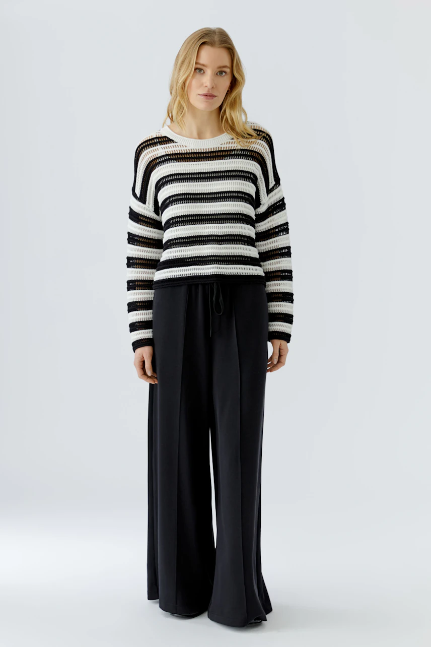 Casual women's pullover: Woman in a striped knit pullover with wide black pants, standing confidently.