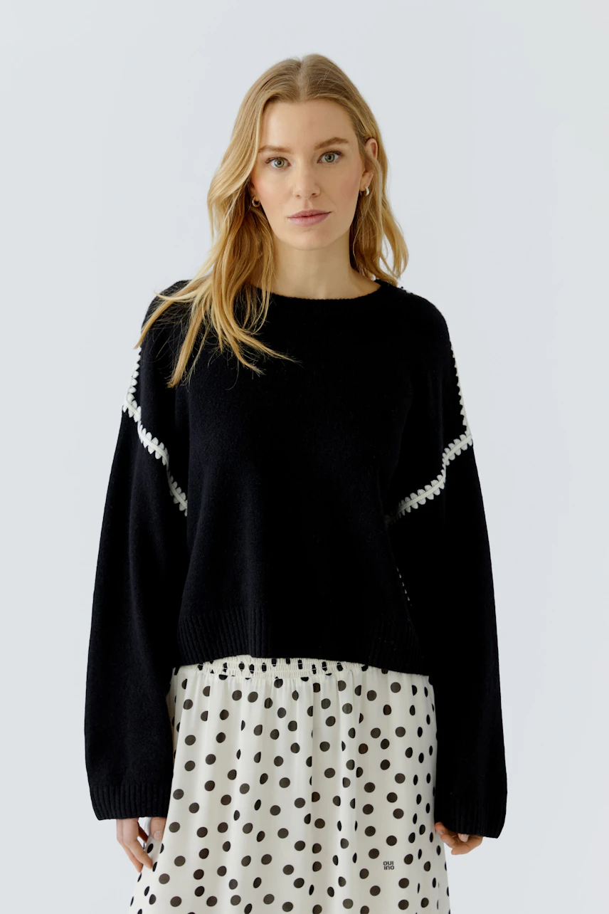 Casual women's pullover: Woman in black pullover with white accents, paired with a polka dot skirt.