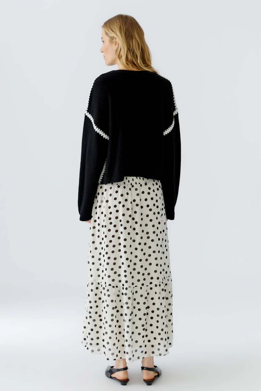 Casual women's pullover: Woman in a black pullover with white accents, paired with a polka dot skirt.