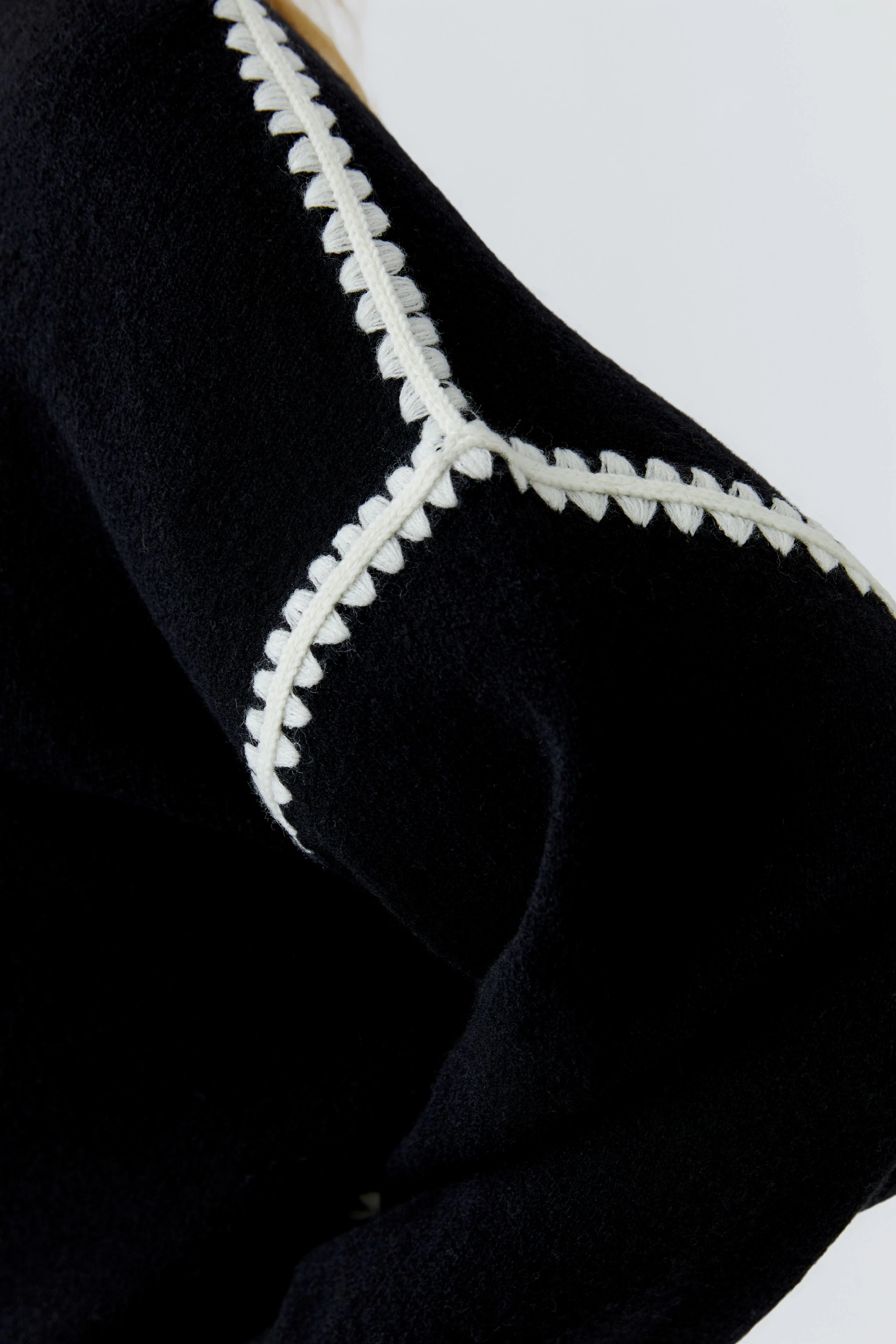 Schwarzer Pullover mit weißem Ziernaht-Detail, Fokus auf Textur und Design.