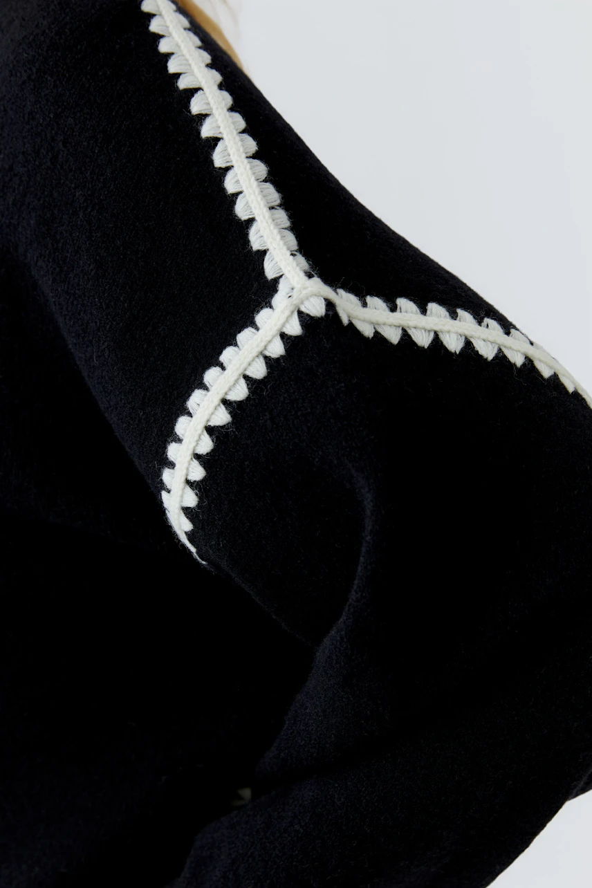 Black pullover with white stitched details, showcasing a modern and stylish design.