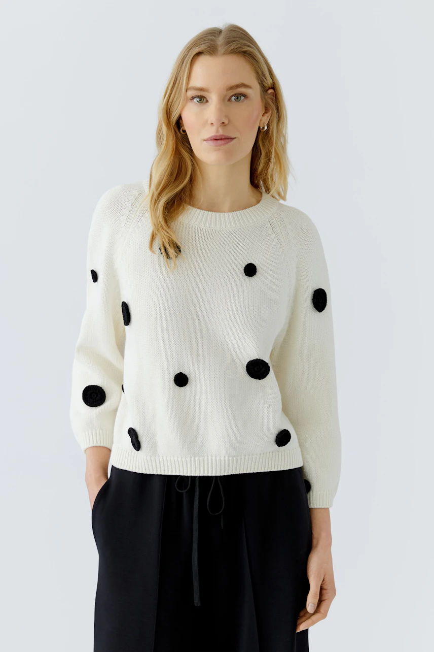 Casual women's pullover: Woman in white pullover with black dots, relaxed fit, and simple design.