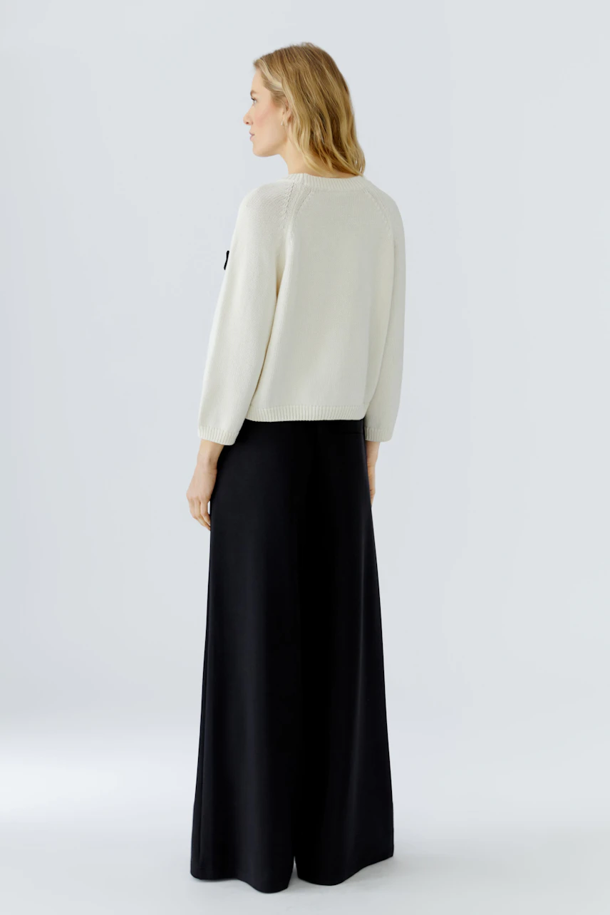 Casual women's pullover: Woman in a cream pullover and black wide-leg pants, viewed from the side.