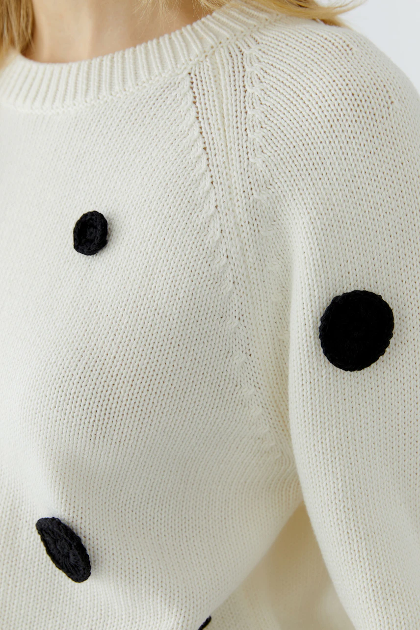 Woman in a cream pullover with black polka dots, showcasing a casual and playful style.