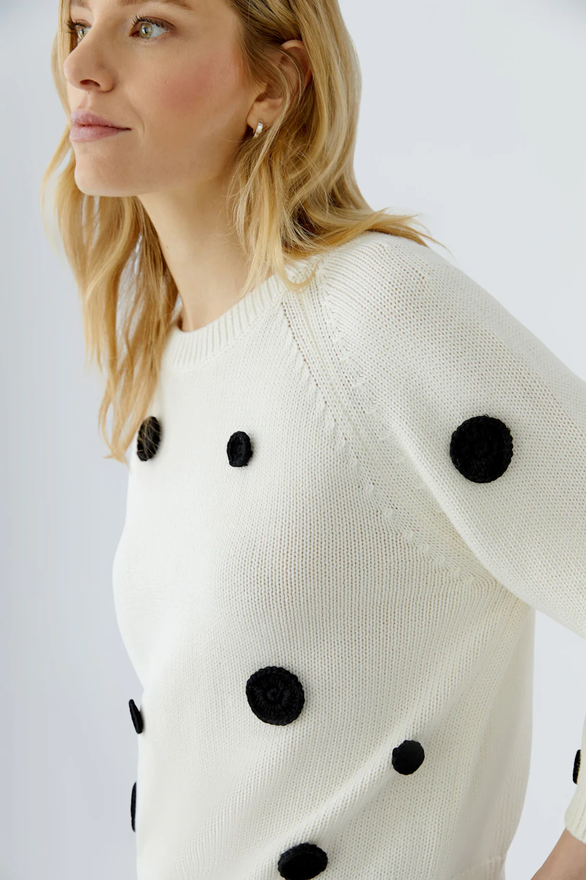 Woman in a white pullover with black polka dots, looking to the side. Casual and stylish design.