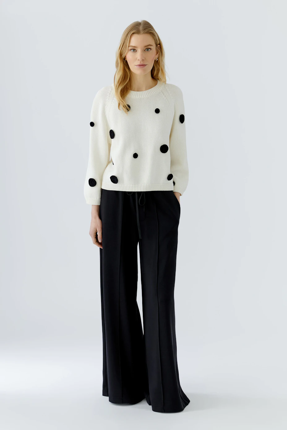 White pullover with black polka dots, displayed on a hanger. Casual and stylish design.