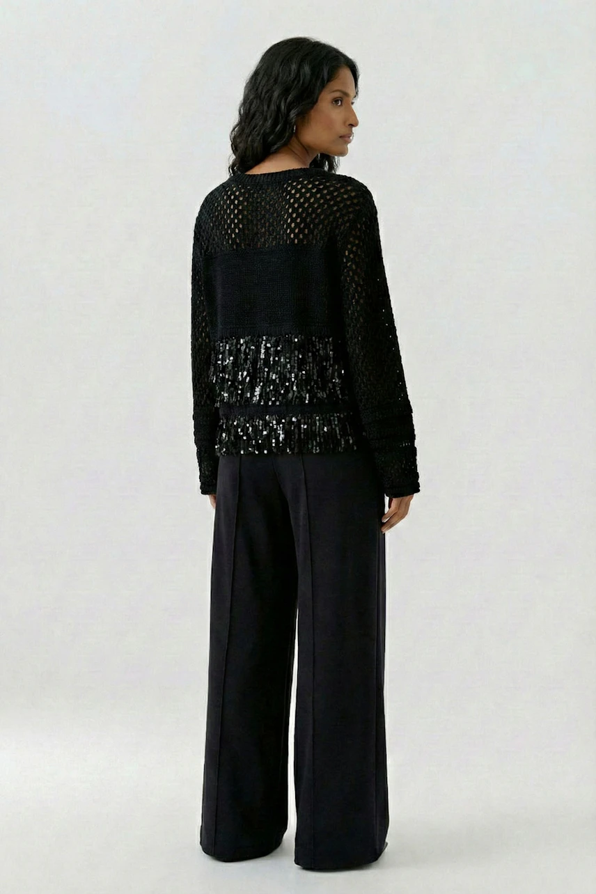 Woman in black pullover with mesh design and sequin details, paired with wide-leg pants.