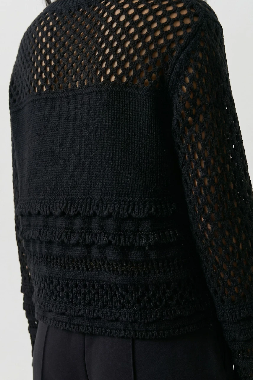 Damen-Pullover: Frau im schwarzen Pullover mit Fransen und Pailletten, kombiniert mit dunkler Hose.
