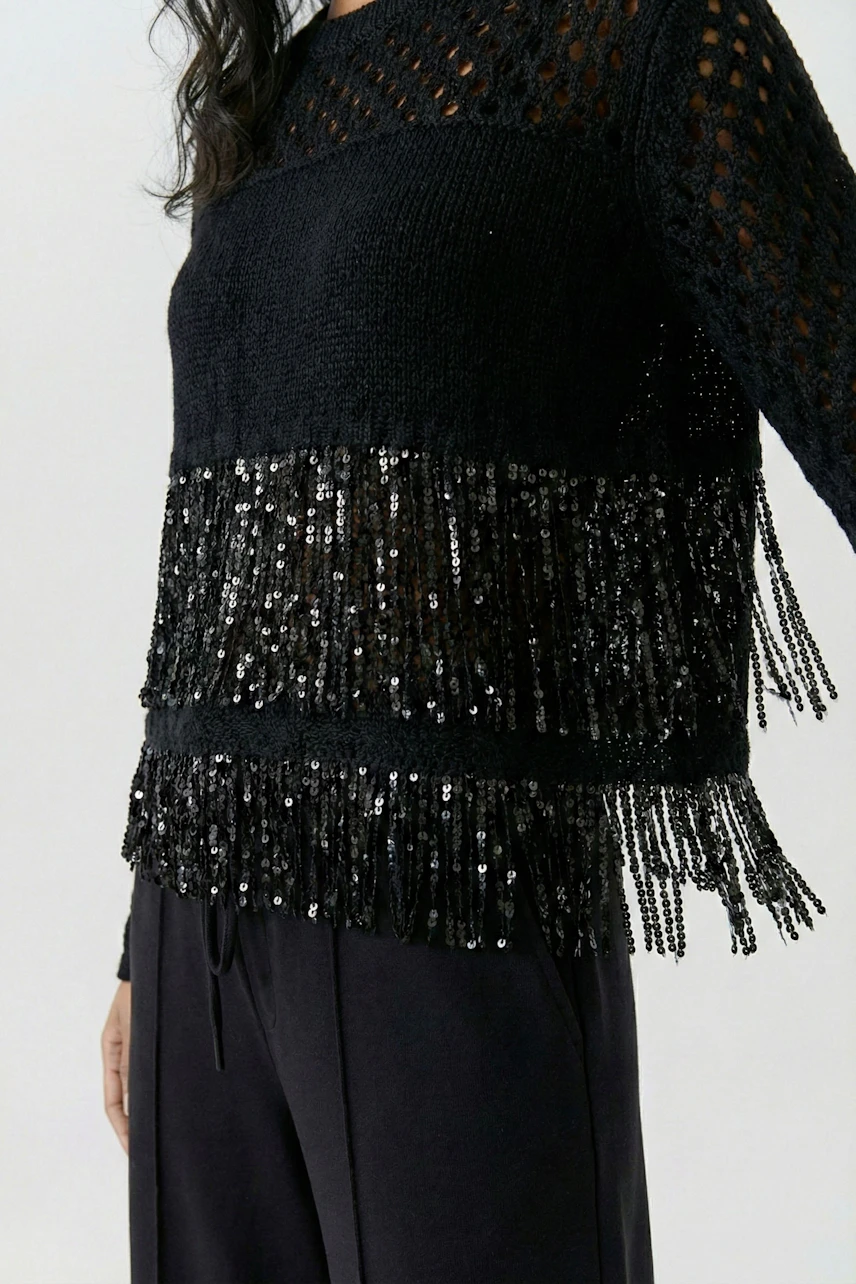 Woman in a black pullover with sequin fringe, paired with dark pants, showcasing a chic, modern style.