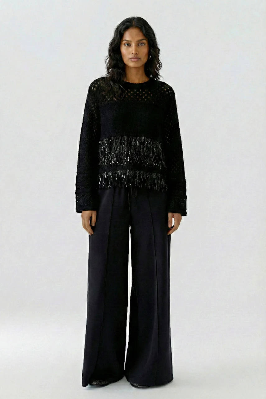 Woman in a black pullover with fringe details, paired with wide-leg pants, standing confidently.