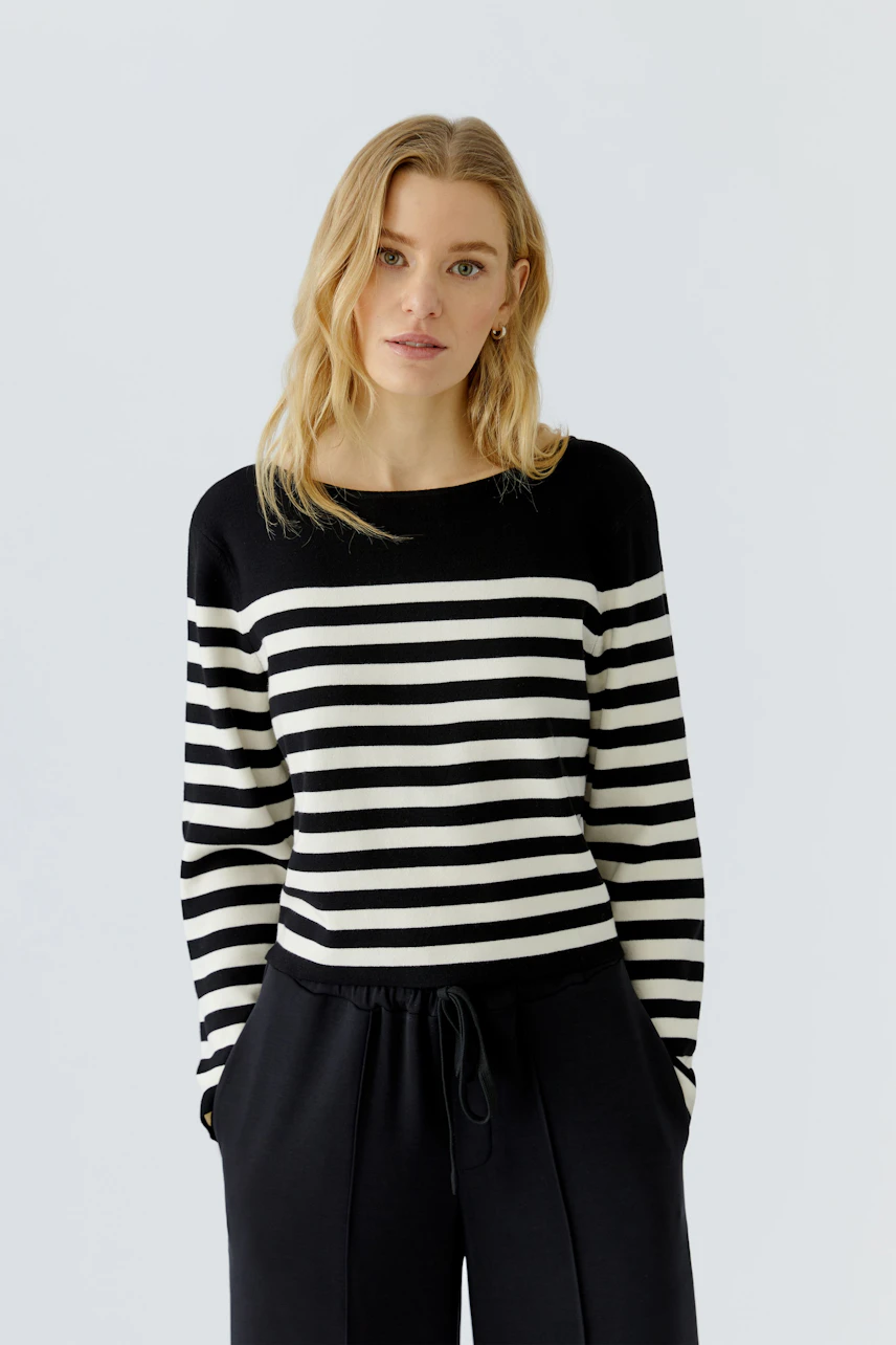 Casual women's pullover: Woman in black and white striped pullover with relaxed black pants, looking confident.