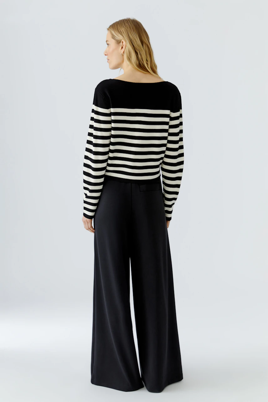 Casual women's pullover: Woman in black and white striped pullover with wide-leg black pants, seen from behind.