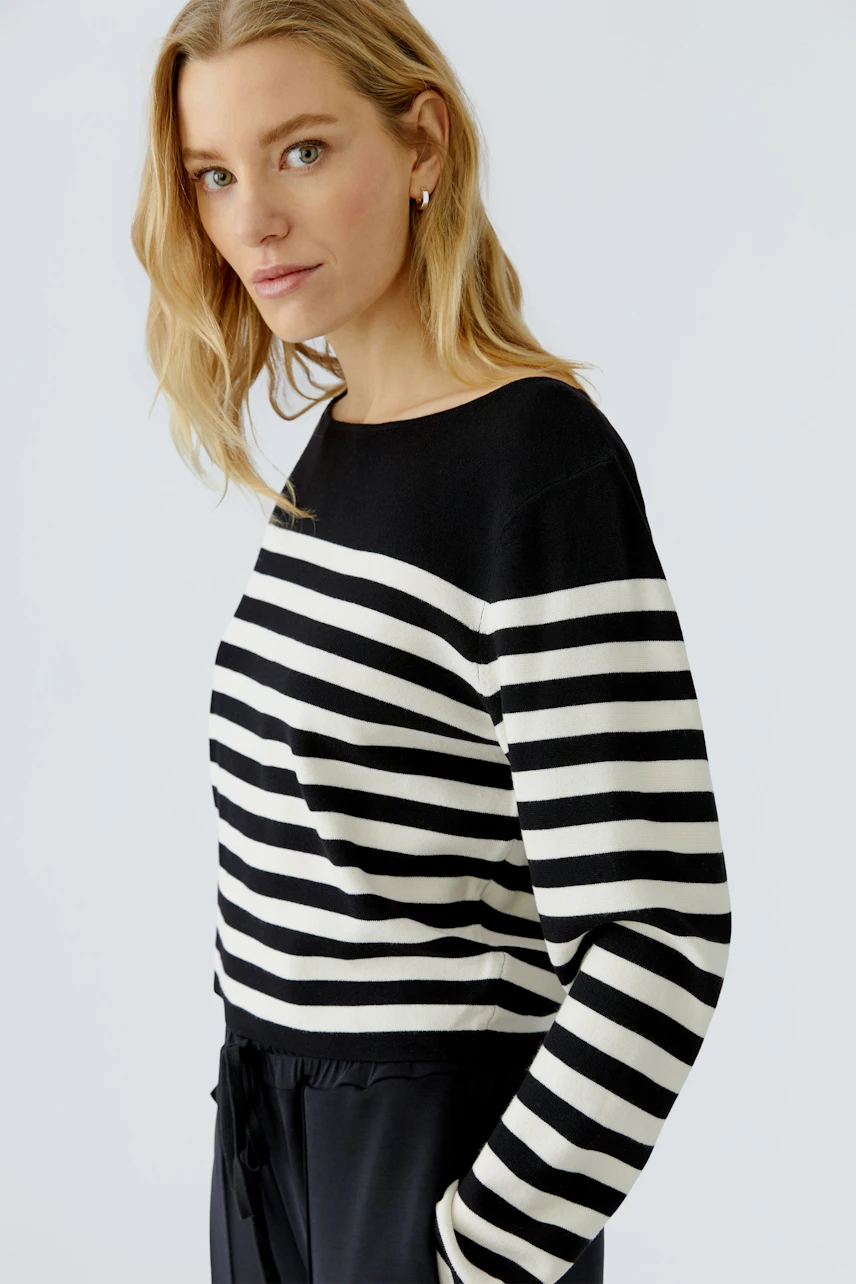 Casual women's pullover: Woman in black and white striped pullover, relaxed fit, looking confidently.