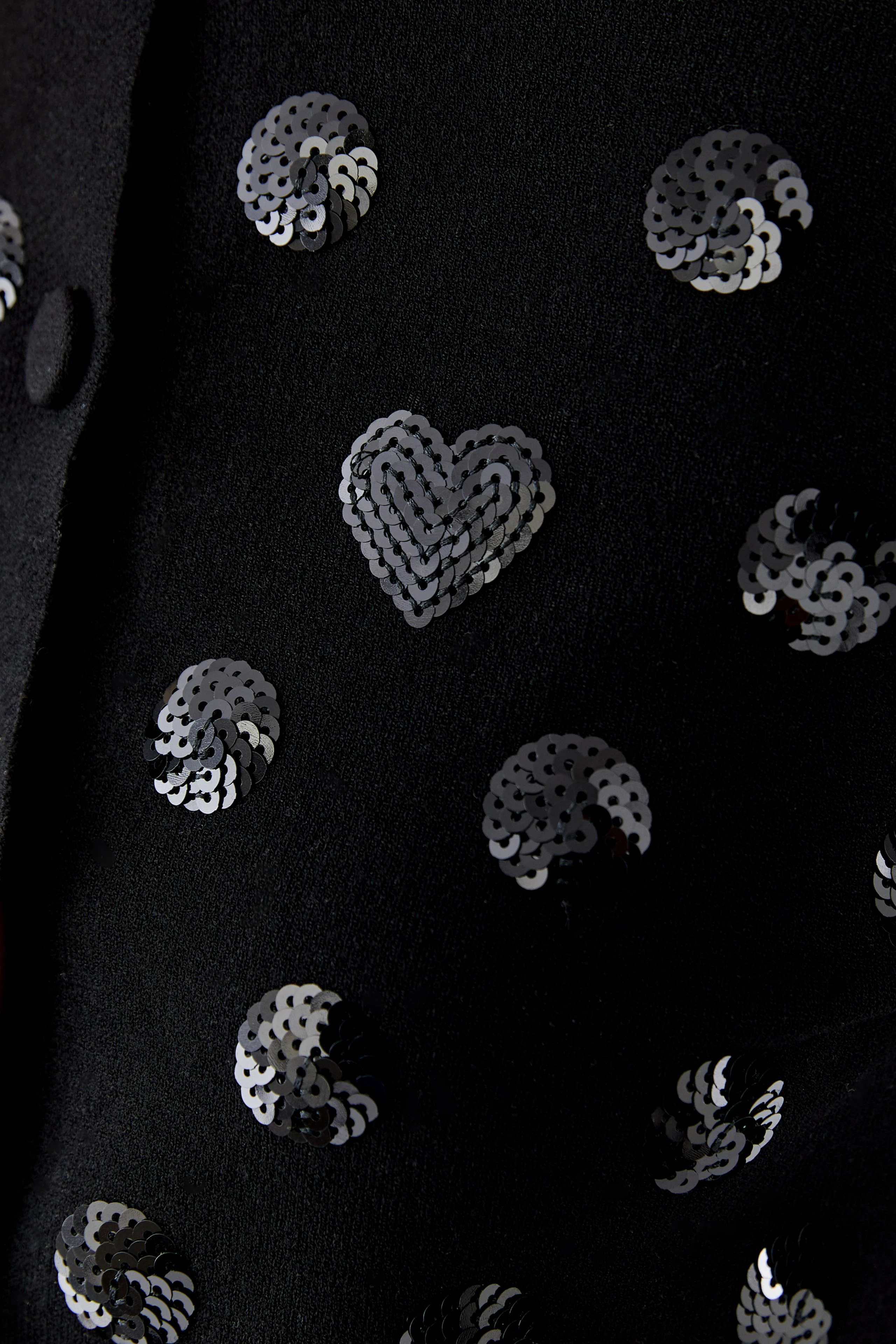 Schwarze Strickjacke mit Pailletten: Herz- und Kreisdesigns verleihen dem Look einen verspielten Touch.
