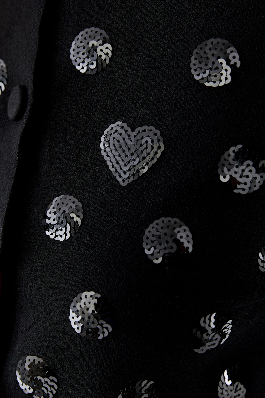Black cardigan with sequin heart and swirl patterns, adding a playful touch to any outfit.