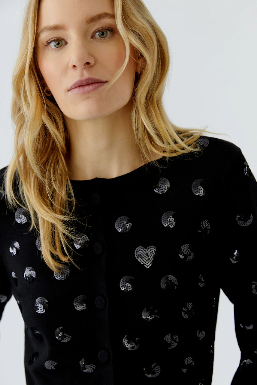 Woman in a black cardigan with silver patterns, looking confidently. Casual and stylish knitwear.
