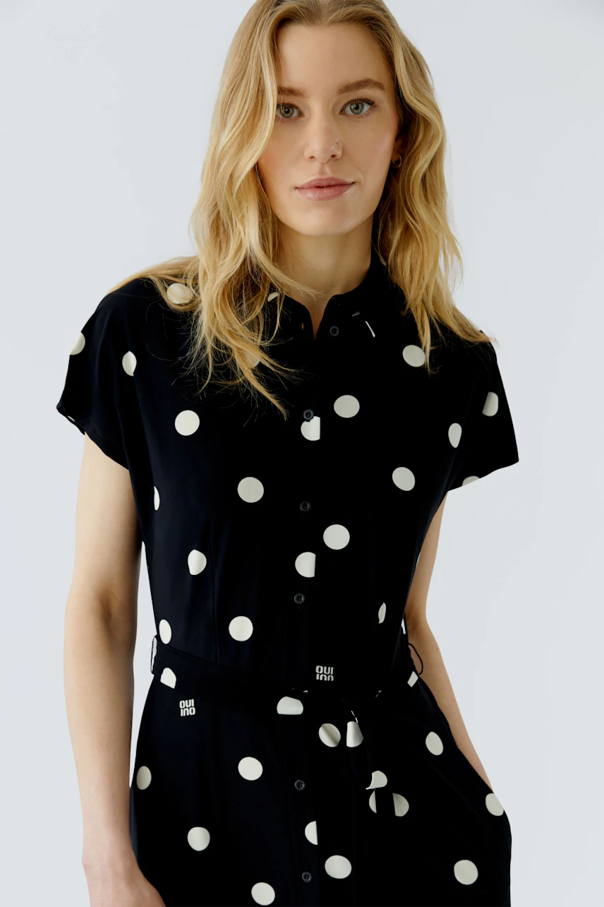 Schwarzes Damen-Kleid: Frau im gepunkteten Kleid mit kurzen Ärmeln und Knopfleiste, lässig und modern.