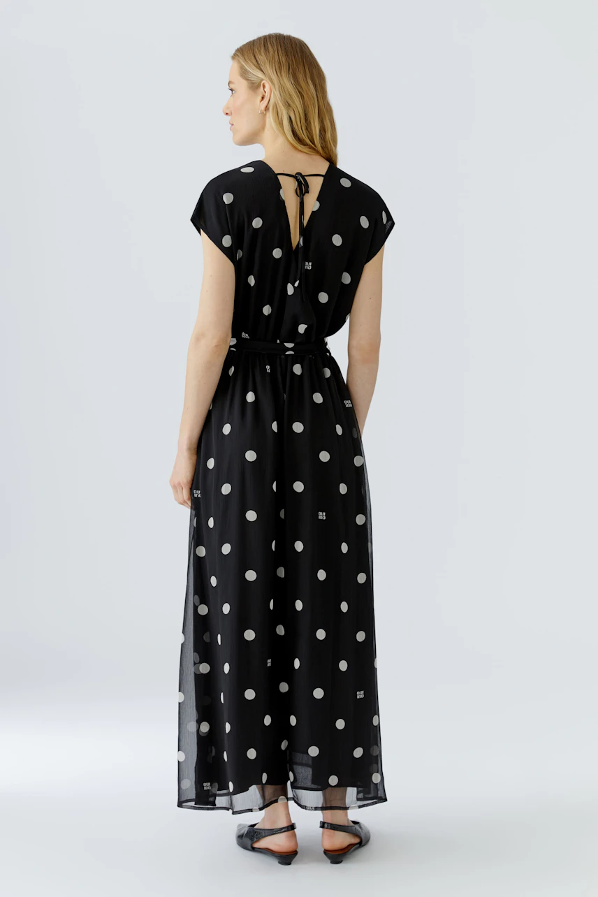 Schwarzes Maxikleid mit weißen Punkten: Frau von hinten im ärmellosen Kleid mit Bindegürtel.