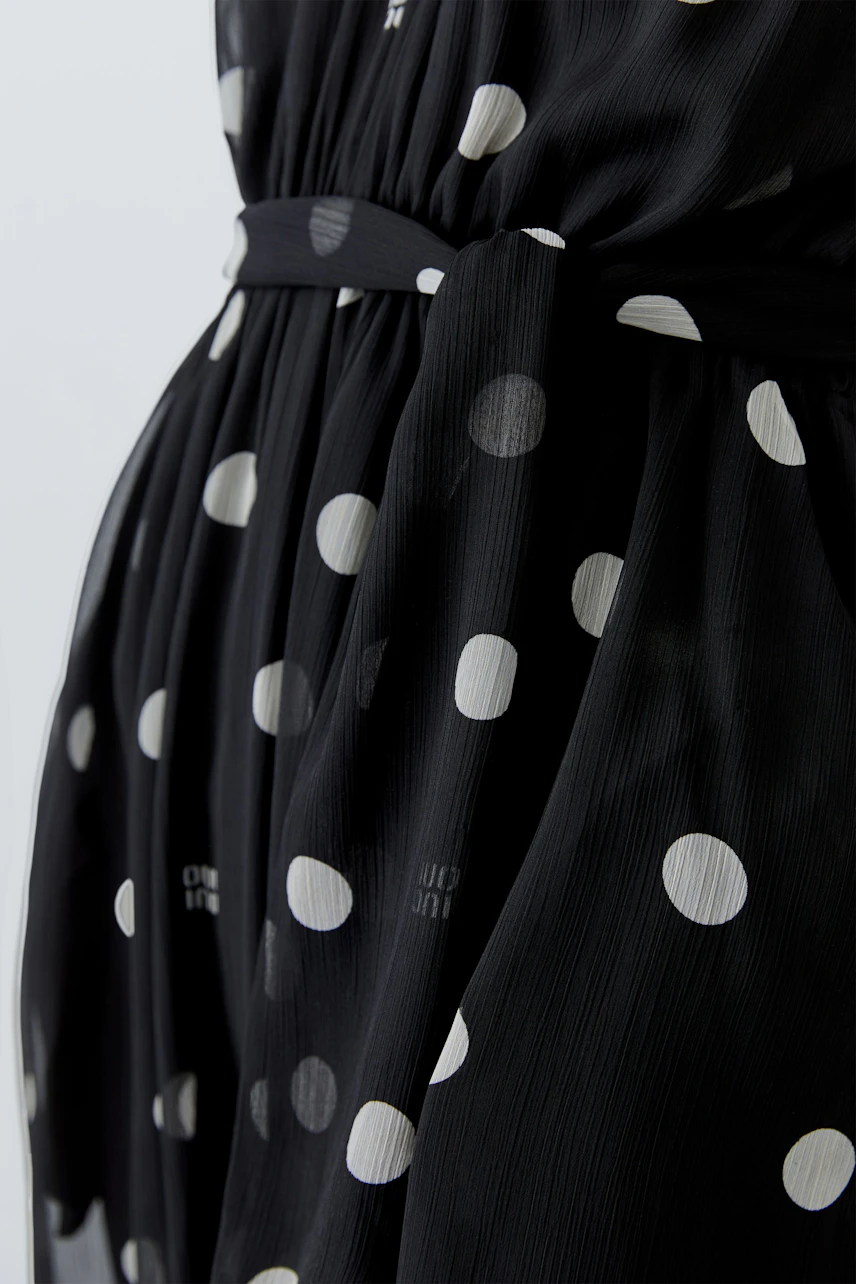 Schwarzes Maxikleid mit weißen Punkten, fließender Stoff, betont die Taille. Ideal für lässige Anlässe.