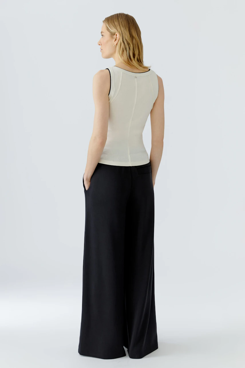 Woman in a white tank top and black wide-leg pants, viewed from the back, showcasing casual style.