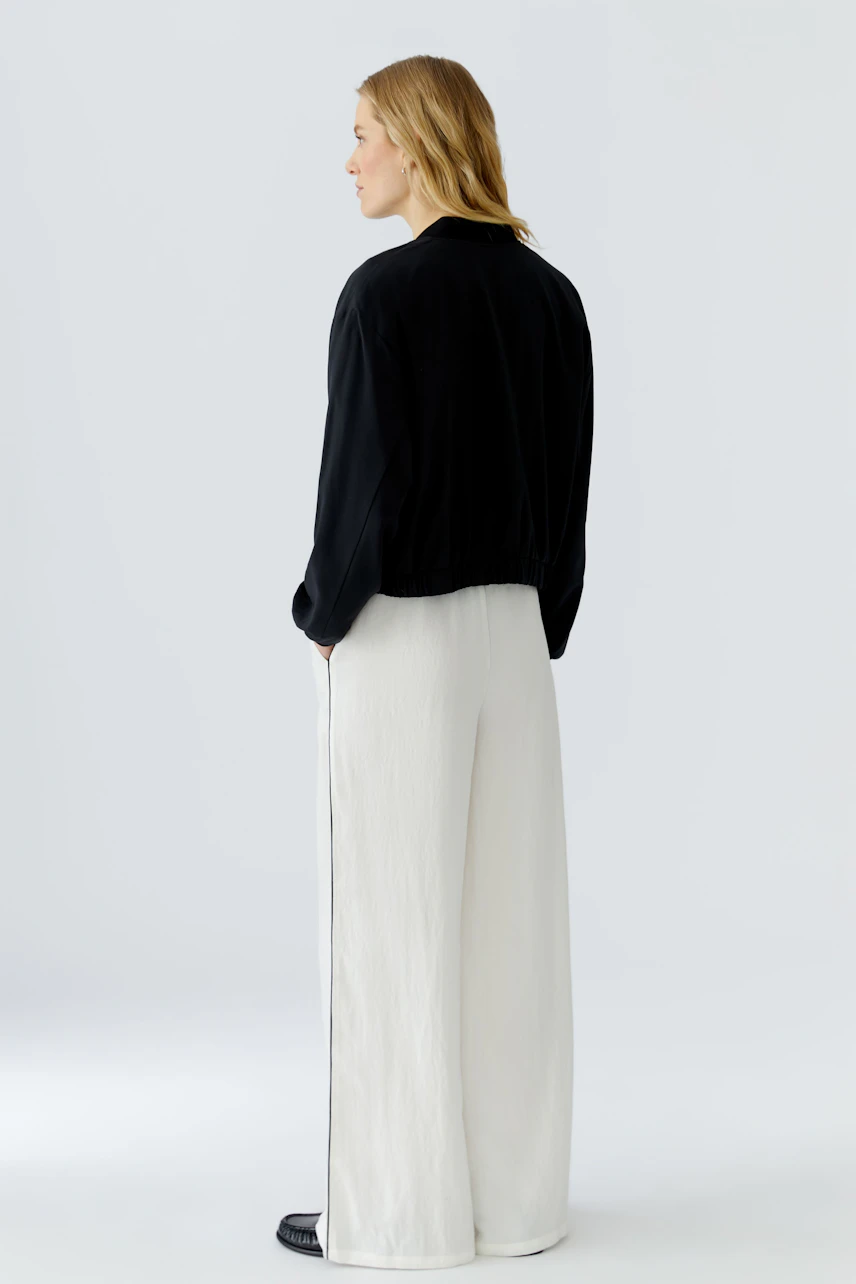 Woman in black blouson and white wide-leg pants, side view. Casual and modern style.