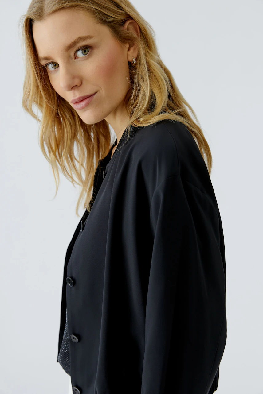 Woman in a black blouson, looking confidently. Casual style with button details.