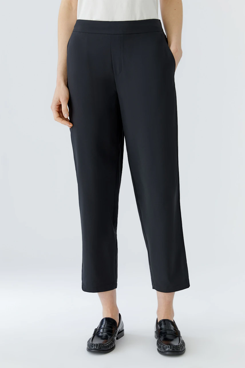 Casual women's pants: Woman in black pants with a white top and loafers, standing confidently.