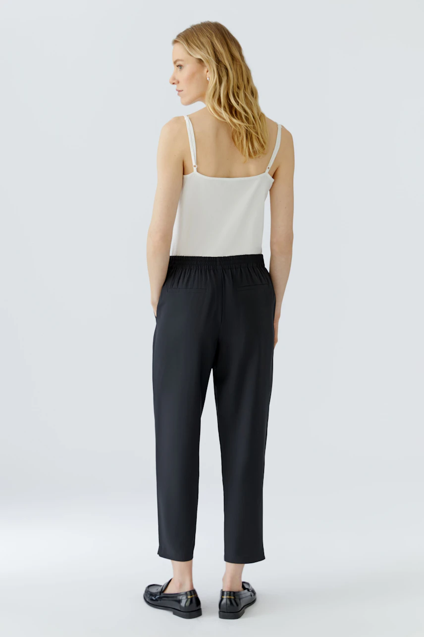 Casual women's pants: Woman in black pants and white top, standing with relaxed posture.