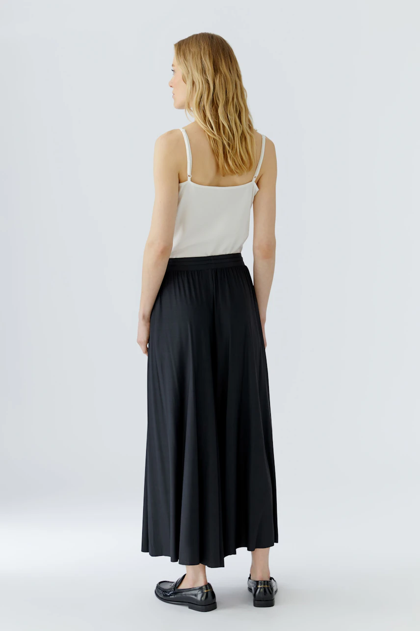 Woman in black culotte and white top, standing with back view, showcasing relaxed fit and flowy design.