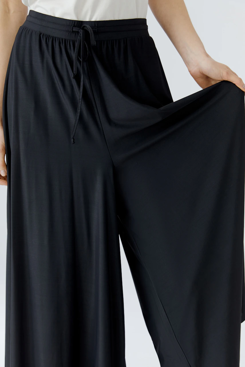 Woman in black culotte pants, showcasing wide leg fit and drawstring waist, paired with a white top.