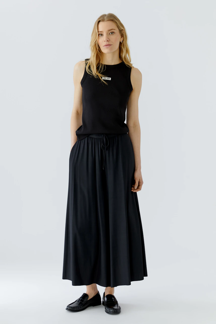 Casual culotte: Woman in a black sleeveless top and flowing black culotte, standing confidently.